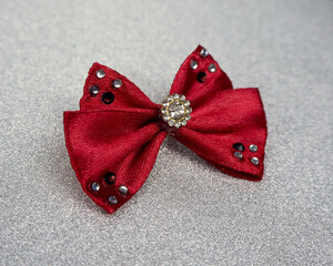 on a silver background lies a burgundy bow with shiny stones in the middle. Christmas. accessories . side view. bows for dogs