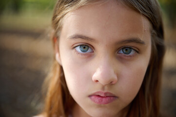 Fototapeta premium Portrait of sad young girl in the autumn park in sunny bright day. Close up.
