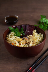 A brown bowl of Korean soup with food sticks on the dark. Japanese ramen noodles with chicken, boiled egg, mushrooms, spring onions and soy sauce. Korean soup. Traditional Asian cuisine. vertical