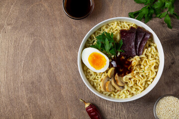 Traditional Asian cuisine. A white bowl of Korean soup with food sticks on the brown. ramen noodles with chicken, boiled egg, mushrooms, spring onions and soy sauce. top view. copy space