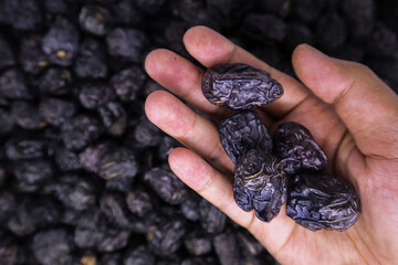 Close-up view of a man's hand holding one large delicious Ajwa dates against the pile of blurred...
