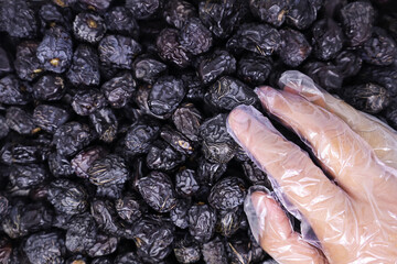 Close-up view of a man's hand wearing plastic food gloves touching a bunch of delicious Ajwa dates to keep the food clean with a pile of Ajwa dates in the background. Healthy Arabic food concept.