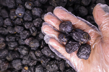 Man's hand using plastic food gloves holding a large group of delicious Ajwa dates to keep food hygienic against the pile of blurred Ajwa dates background. Healthy Arabic food concept.