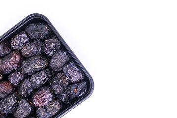 Copy space background of Black food container filled with Pile of large delicious Ajwa dates to keep food hygienic isolated on white background. Arabic healthy food concept. Top view with copy space.