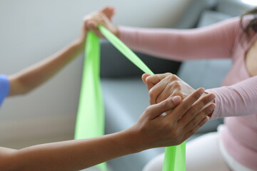 Physiotherapist nurse doing senior female patient physiotherapy to restore arm muscles with elastic bands.