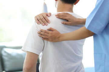 Doctor diagnosing man's shoulder pain in hospital examination room. Nurse doing massage and...