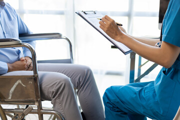 Obraz premium Man with a leg injury in a wheelchair sees a doctor in a hospital for a check-up. Female doctor examining a wheelchair patient in an examination room at a hospital.