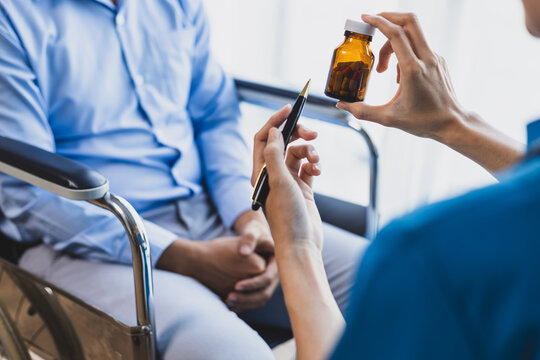 Female Doctor Is Giving Physical Therapy Advice To A Male Patient In A Wheelchair And Taking Medication By A Specialist Doctor.