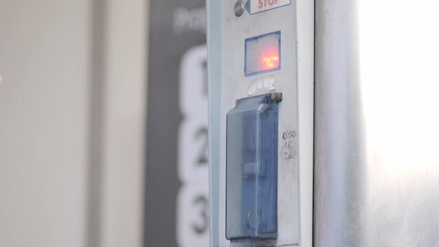 A woman in a manual car wash uses a coin acceptor and holds down a button to start the water supply.