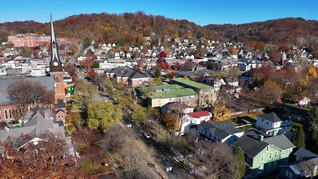 A wide forward aerial establishing shot of a New England-type small town in the autumn season. Church steeple in the foreground, business district in the distance. Pittsburgh suburbs.  	