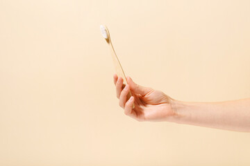 Close-up of a female hand holding a natural wooden toothbrush on a white isolated background....