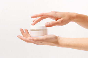 Female fragile hands holding glass transparent mockup jar of face cream on white isolated background. The concept of presenting a new beauty product, skin care, moisturizing and nutrition