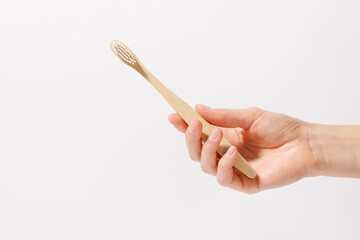 A fragile female hand holding a wooden toothbrush on a white isolated background. Concept of...