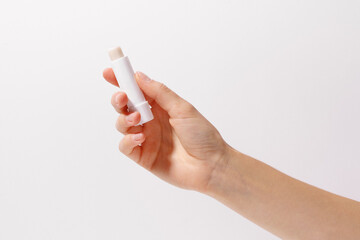 Female hand holding transparent tube of lip balm in white packaging on white isolated background....