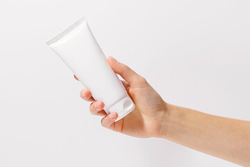 Female hand holding white tube of face and body cream mockup on white isolated background. Image...