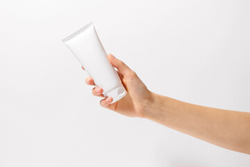 Female hand holding white tube of body or face cream mockup on white isolated background. Beauty...