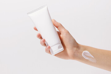 Close-up of a female hand holding a white mockup blank tube of cream on a white isolated...