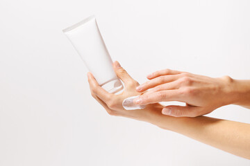 Female hand holding white mockup tube of cream or lotion and applying on skin with fingers on white...