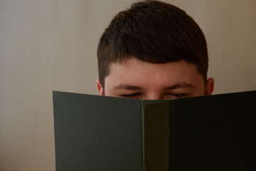 A young man with closed eyes in front of an open book. Difficulty in studying sciences, university education, youth reading books, boring books