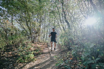 A happy, healthy young man enjoys a day off in nature's wilderness, exploring the green environment on a sunny day. He's running, hiking, and exercising cardio, all while wearing sportswear.