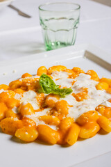 Piatto di gnocchi di patate con zucca, stracciata di bufala e basilico fresco serviti come primo...