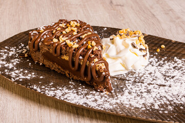 Fetta di torta artigianale ripiena di cioccolato, guarnita con granella di nocciole e crema di cioccolato e accompagnata da panna montata
