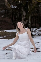 Fototapeta na wymiar happy woman in a white dress sitting on a snowy ground in a forest