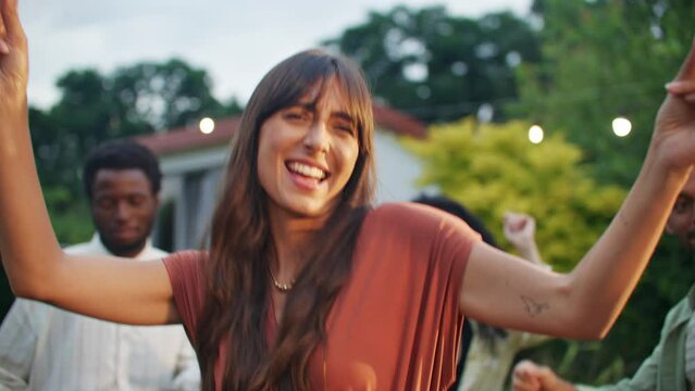 Beautiful smiling woman dancing at center of circle with friends, providing attention and looking at camera. Summertime, dance party at yard in front of house. Celebration, music, joy and fun.
