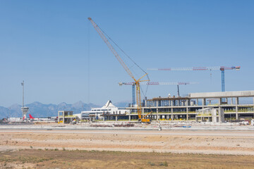 Fototapeta na wymiar Construction of a new airport terminal building, view of cranes machinery and aircraft parked around. Transport hub reconstruction.