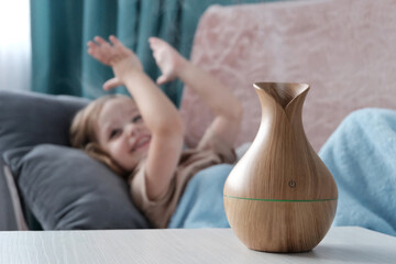 Diffuser wooden jug light electric. In the background, a little blonde girl is happy, clapping her...