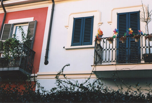 Red And Light Blue House Facade in Milano Old Town, Italy, with Colorful Pinwheels on the Balcony. Film Photography