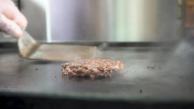 A hamburger patty grilling on a flat top grill and being flipped