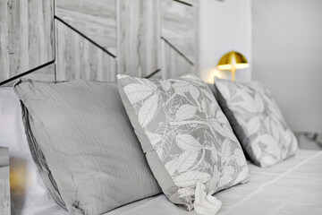 Close up of gray cushions on bed in cozy bedroom illuminated by bedside lamp