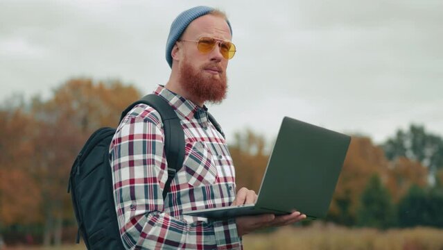 Young tourist with black backpack exploring unfamiliar territory on gloomy autumn day using modern technologies. Blurred background of orange trees. High quality 4k footage