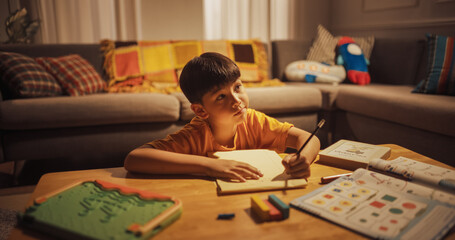 Evening Portrait of the Smart Young Boy Diligently Doing Homework in the Living Room. Focused Kid Learning, Studying for best Grade, Writing Answers for Math. High Achievement Korean Child