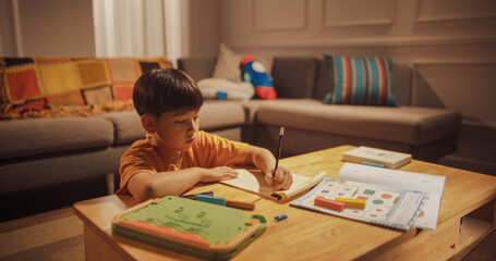 Evening Portrait of the Smart Young Boy Diligently Doing Homework in the Living Room. Focused Kid Learning, Studying for best Grade, Writing Answers for Math. High Achievement Korean Child