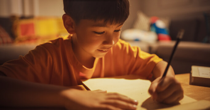 Evening Portrait of Smart Young Boy Doing Homework in the Living Room. Focused Kid Thinking Real Hard on his Math lesson, writing Test answers, Learning, Studying for best Grades