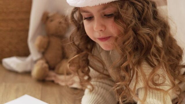 A child in a Santa hat draws a picture on paper with a pencil, holiday concept