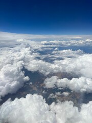 Vertical aerial view of a rural landscape enveloped in puffy clouds in blue sky background