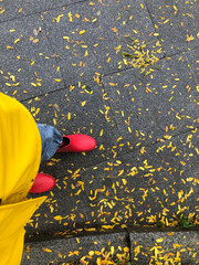 person wearing red boots and yellow raincoat walking on dried autumn leaves