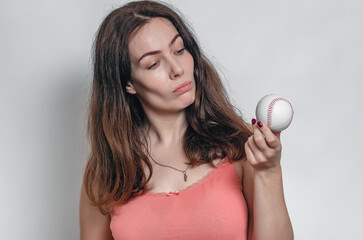 Dark-haired woman in a pink T-shirt holds a baseball in her hand. Looks at the ball.