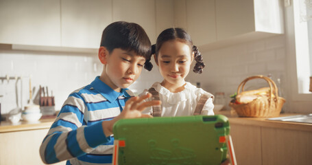 Portrait of Two Korean Kids Using a Digital Tablet During Weekend in The Kitchen. Two Cute Asian Siblings Watching Educational Content Online, Sharing the Gadget, and Enjoying Their Time