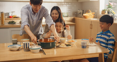 Happy Korean Family of Four Enjoying a Delicious Meal Together in Their Kitchen at Home. They are Sharing a Traditional Meal Made with Love and Care. Children Excited for Food