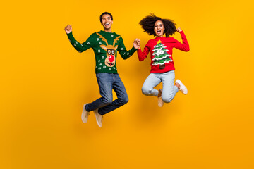 Fototapeta na wymiar Full body photo of two delighted american people jumping hold arms raise fists x-mas sale isolated on yellow color background
