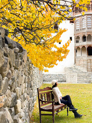 A young woman is sitting alone on a wooden chair. To admire the atmosphere of autumn The leaves turn beautiful shades of yellow-orange and look very peaceful.