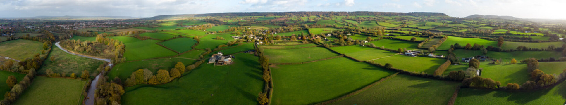 Aerial panoramic landscape of the English countryside. Green fields and rolling hills with farms and the river Otter in view. Devon landscape. Vibrant idyllic panoramic image of countryside life.