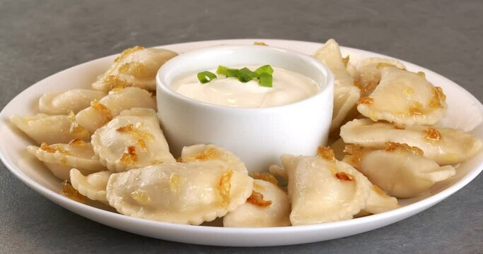 Dumplings with fried onions and bowl with sour cream. Varenyky, vareniki, pierogi, pyrohy with filling.
Close-up footage on the rotating table.