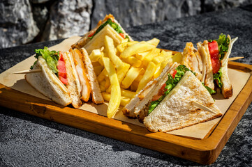 Close-Up of Irresistible Delights. Wooden board featuringclub sandwiches, carefully crafted with layers of fresh ingredients. Accompanied by golden French fries, perfect for food enthusiasts.