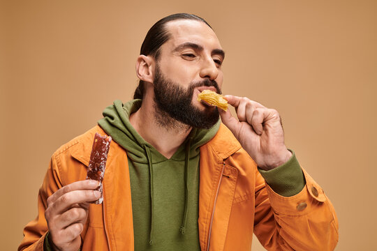 arabic bearded man and biting baklava and holding cevizli sucuk on beige backdrop, turkish delights