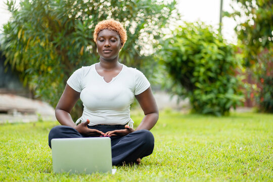 image of beautiful african lady seated with crossed legs, laptop in front in a quiet space- black lady enjoying online yoga poses